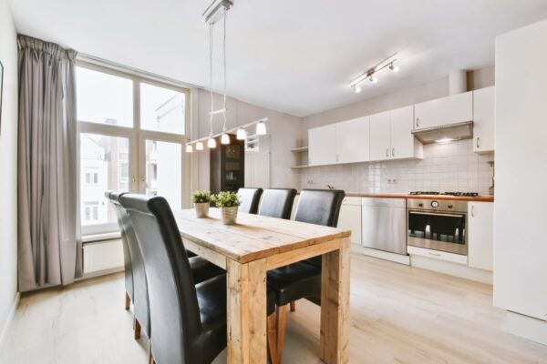 Przestronny, jasny salon z aneksem kuchennym, prezentujący najważniejsze aspekty lokalizacji mieszkania: dobre oświetlenie naturalne i nowoczesne wyposażenie.