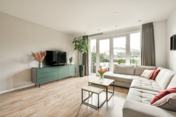 Jasny i przytulny salon z dużymi oknami pokazuje, jak przyciągnąć kupujących nieruchomość – wystarczy zadbać o odpowiednie umiejscowienie mebli i dodatków.