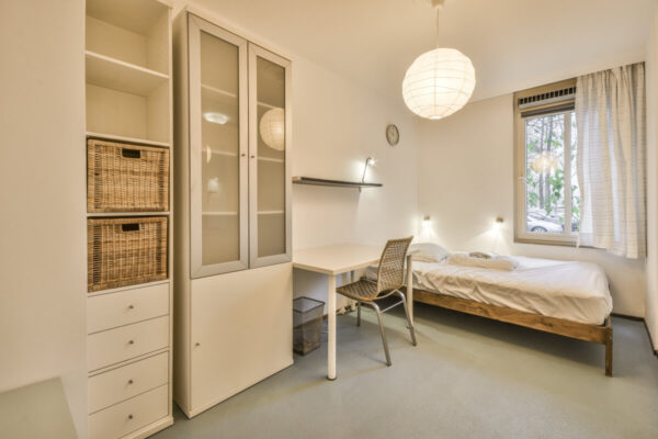 Pokój z biurkiem i łóżkiem ilustruje typowe wnętrze do wynajęcia, a proces sprzedaży nieruchomości czas trwania bywa kluczowy dla kupujących.